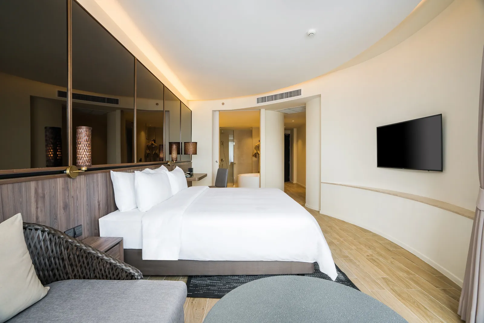 Seaview Grand Deluxe room with a king bed, curved feature wall, wall-mounted TV and an ensuite bathtub visible through the doorway